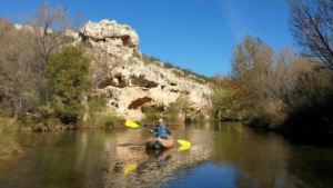 Man on Verde River in an orange inflatable kayak with a yellow paddle. The water is calm.