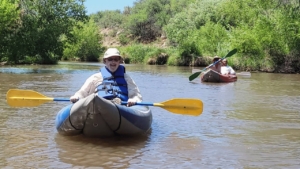 Man with hat on in a blue inflatable kayak on the Verde River. Holding a blue and yellow paddle