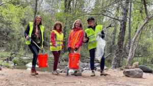 Four volunteers hold up buckets and trash bags for litter clean-up