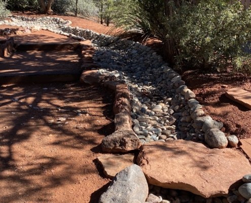 A small walking bridge made of a flat rock spans over the ditch, part of a passive rainwater harvesting system