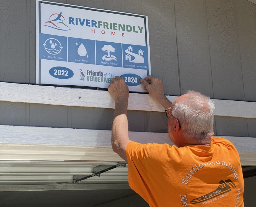 A man proudly affixes a 2024 participation sticker onto a River Friendly Living sign