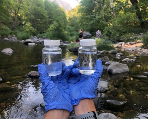 volunteer with blue gloves holding up two little bottles of river water