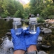 volunteer with blue gloves holding up two little bottles of river water